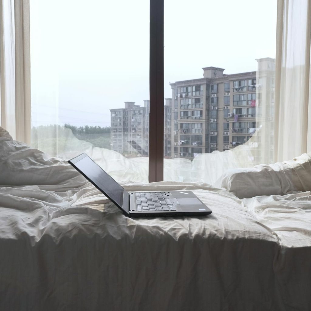 Open laptop on a bed with a view of modern buildings through a Shanghai window.