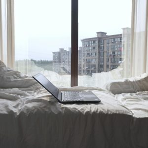 Open laptop on a bed with a view of modern buildings through a Shanghai window.