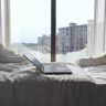 Open laptop on a bed with a view of modern buildings through a Shanghai window.