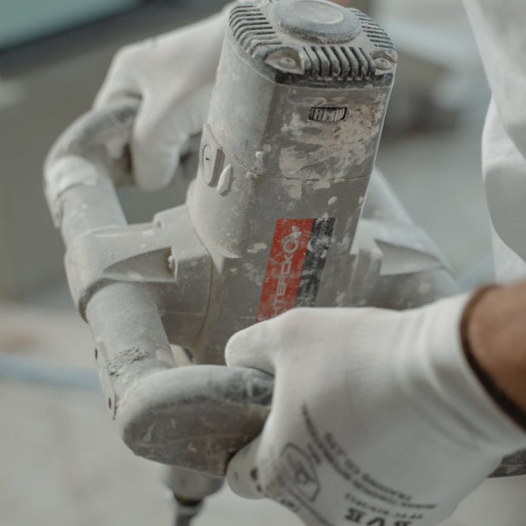 Close-up view of industrial worker's hands using a power mixer tool indoors.