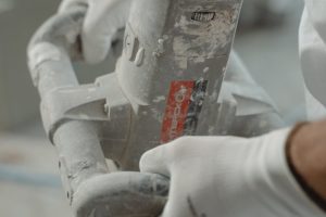 Close-up view of industrial worker's hands using a power mixer tool indoors.
