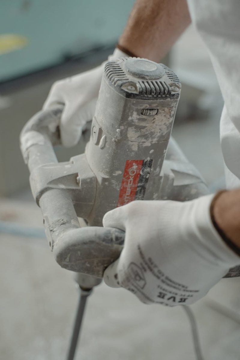 Close-up view of industrial worker's hands using a power mixer tool indoors.
