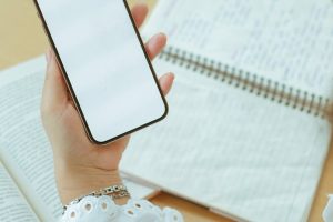 Close-up of a woman's hand holding a blank smartphone over open notebooks, ideal for mockup designs.