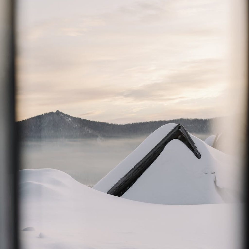 A scenic winter landscape of a snow-laden roof and misty mountains at sunrise.