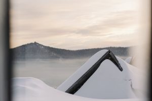 A scenic winter landscape of a snow-laden roof and misty mountains at sunrise.