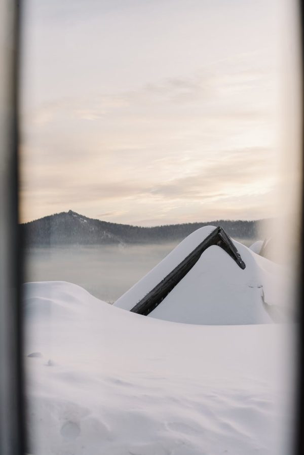 A scenic winter landscape of a snow-laden roof and misty mountains at sunrise.