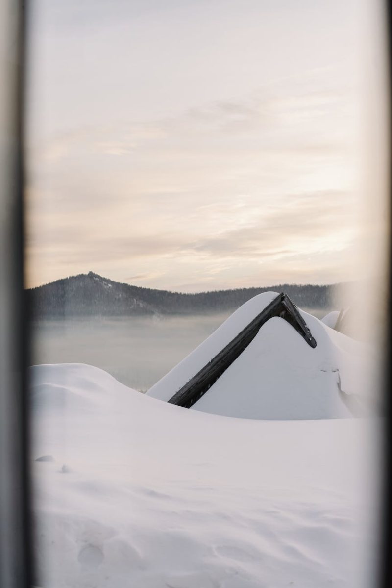 A scenic winter landscape of a snow-laden roof and misty mountains at sunrise.