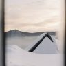 A scenic winter landscape of a snow-laden roof and misty mountains at sunrise.