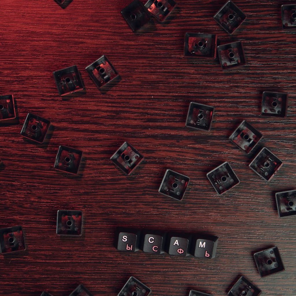 Scattered keyboard keys spelling 'SCAM' on a red-lit wooden surface, symbolizing online fraud.