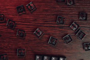 Scattered keyboard keys spelling 'SCAM' on a red-lit wooden surface, symbolizing online fraud.