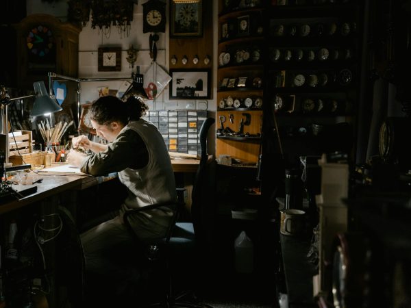 A watchmaker meticulously repairing watches in a dimly lit workshop filled with clocks and tools.