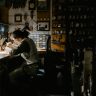 A watchmaker meticulously repairing watches in a dimly lit workshop filled with clocks and tools.